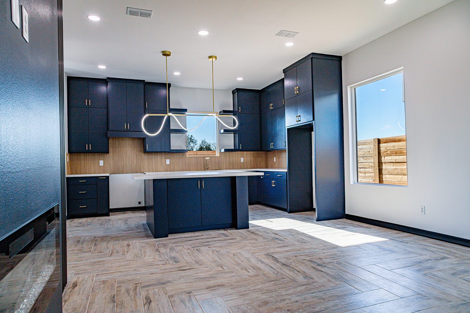 Kitchen with navy cabinetry, gold hardware, wood backsplash, and herringbone tile floor