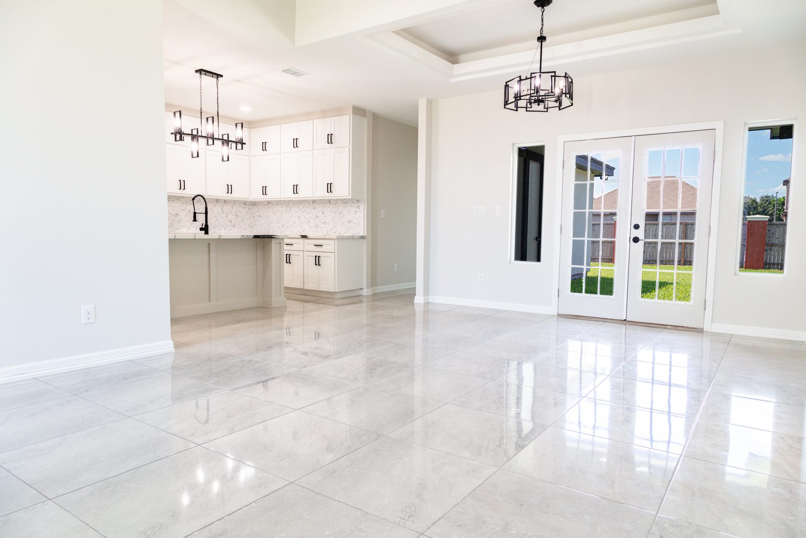 Open-concept living and kitchen with tray ceiling, French doors, and polished tile floor