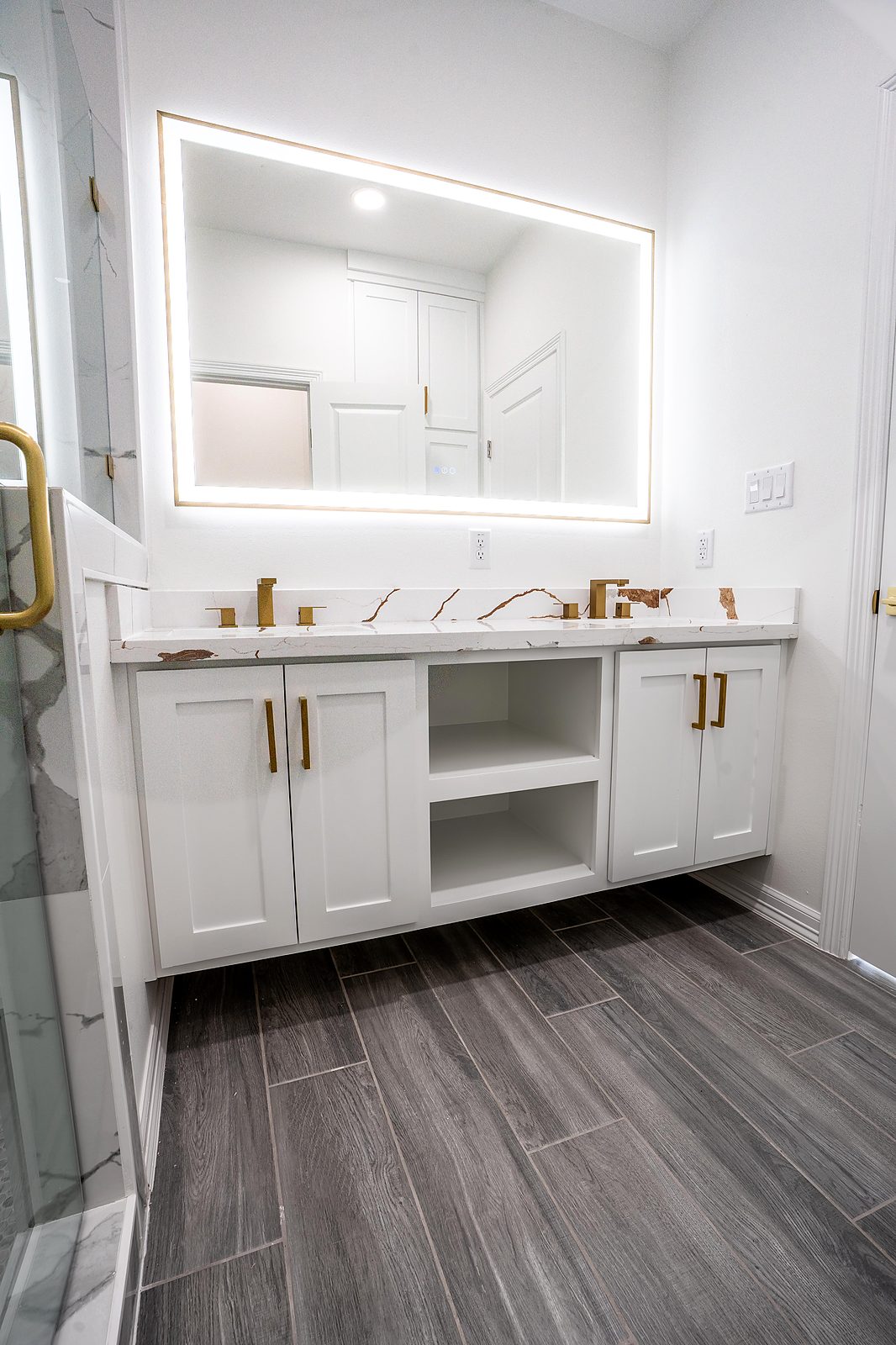 Primary bath with double vanity, backlit mirror, and wood-look tile
