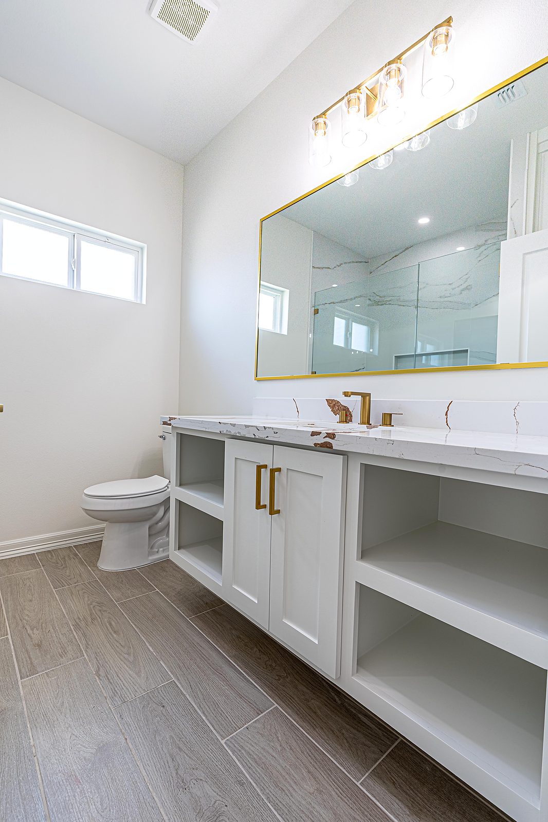 Bathroom with gold-framed lit mirror, quartz double vanity, and wood-look floor