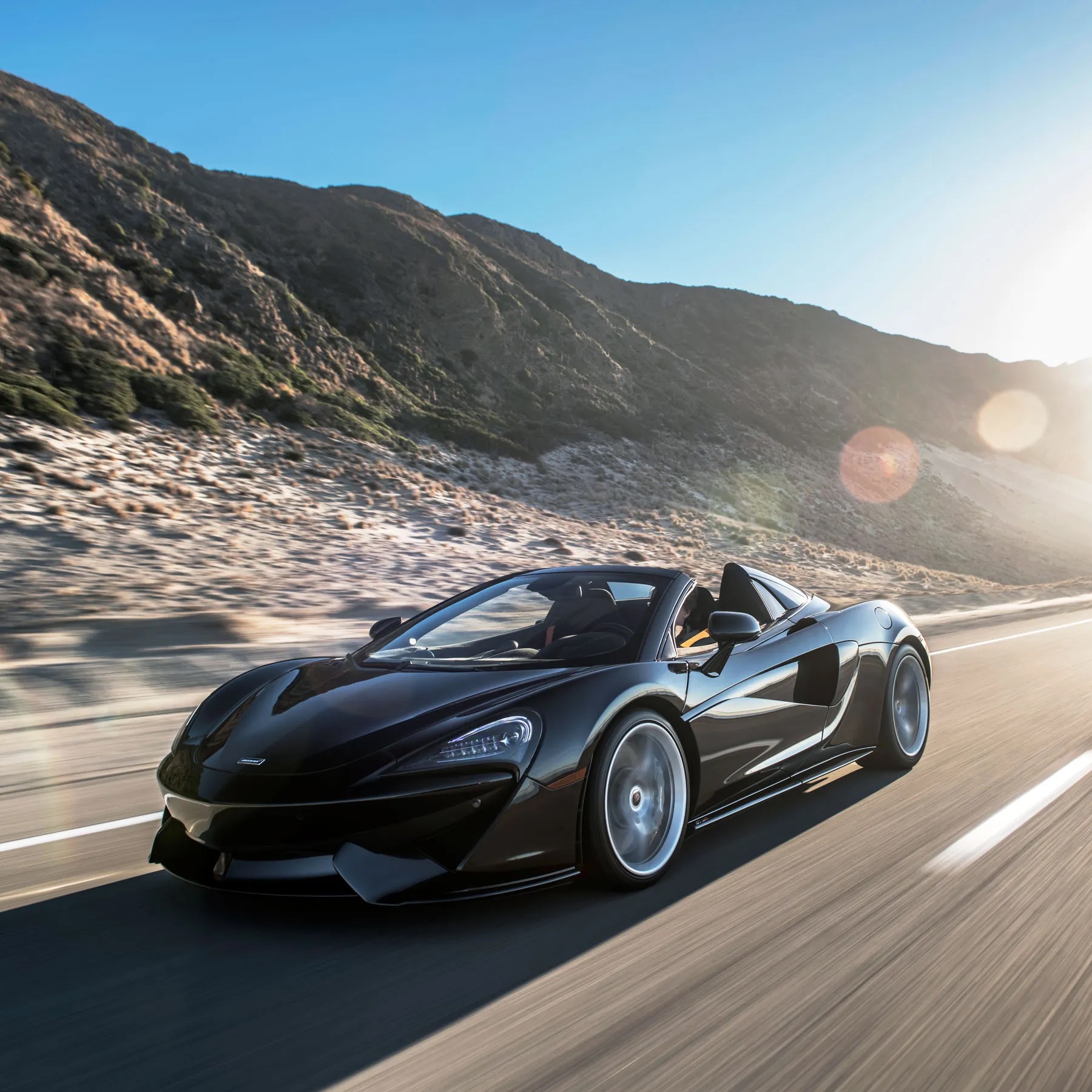 A red high performance sports car driving fast on a winding coastal road with ocean views