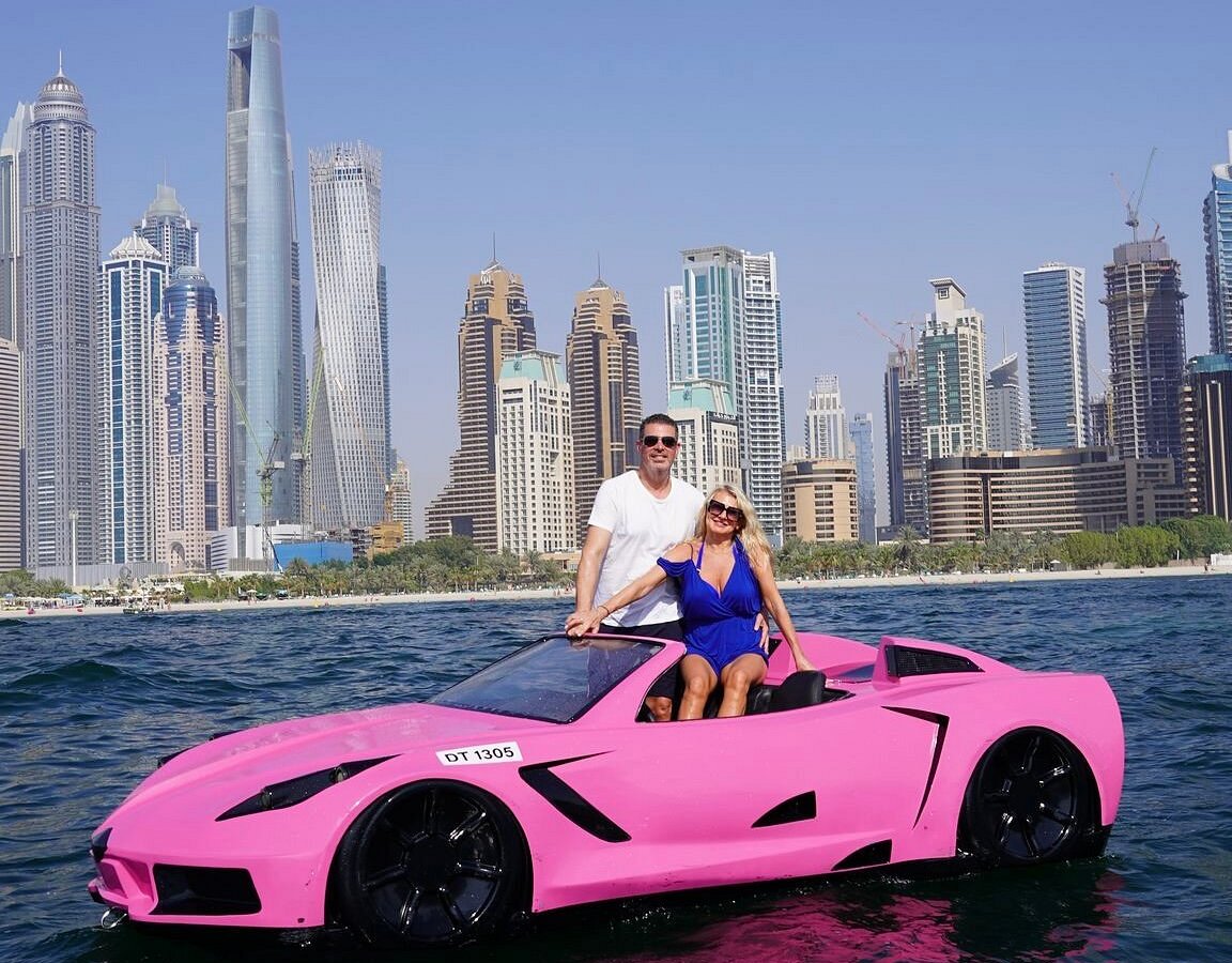 Excited couple cheering with hands up while riding in a luxury jet car on a sunny day in Orlando.