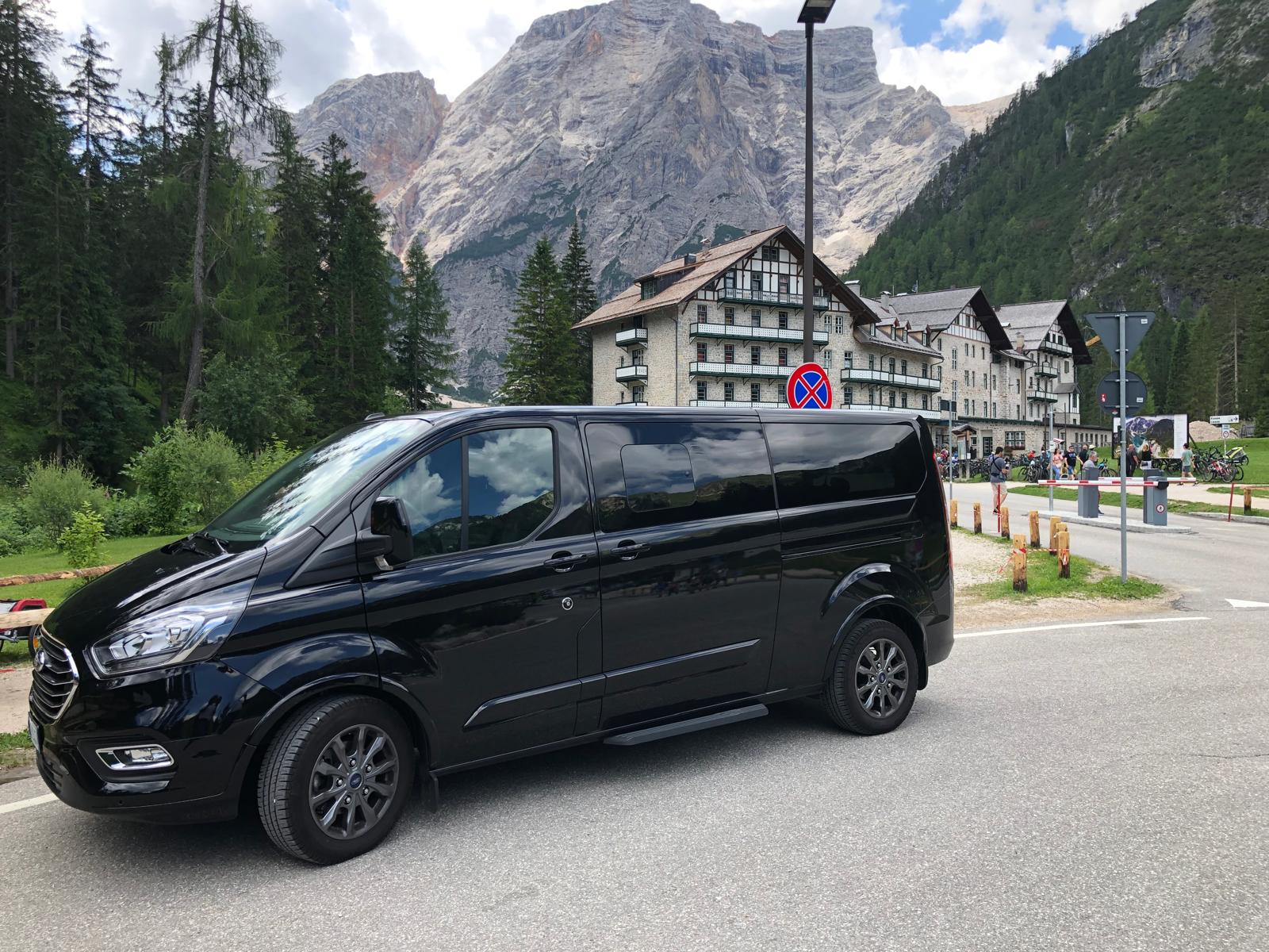 Luxury black shuttle van driving through South Tyrol mountain road at sunset