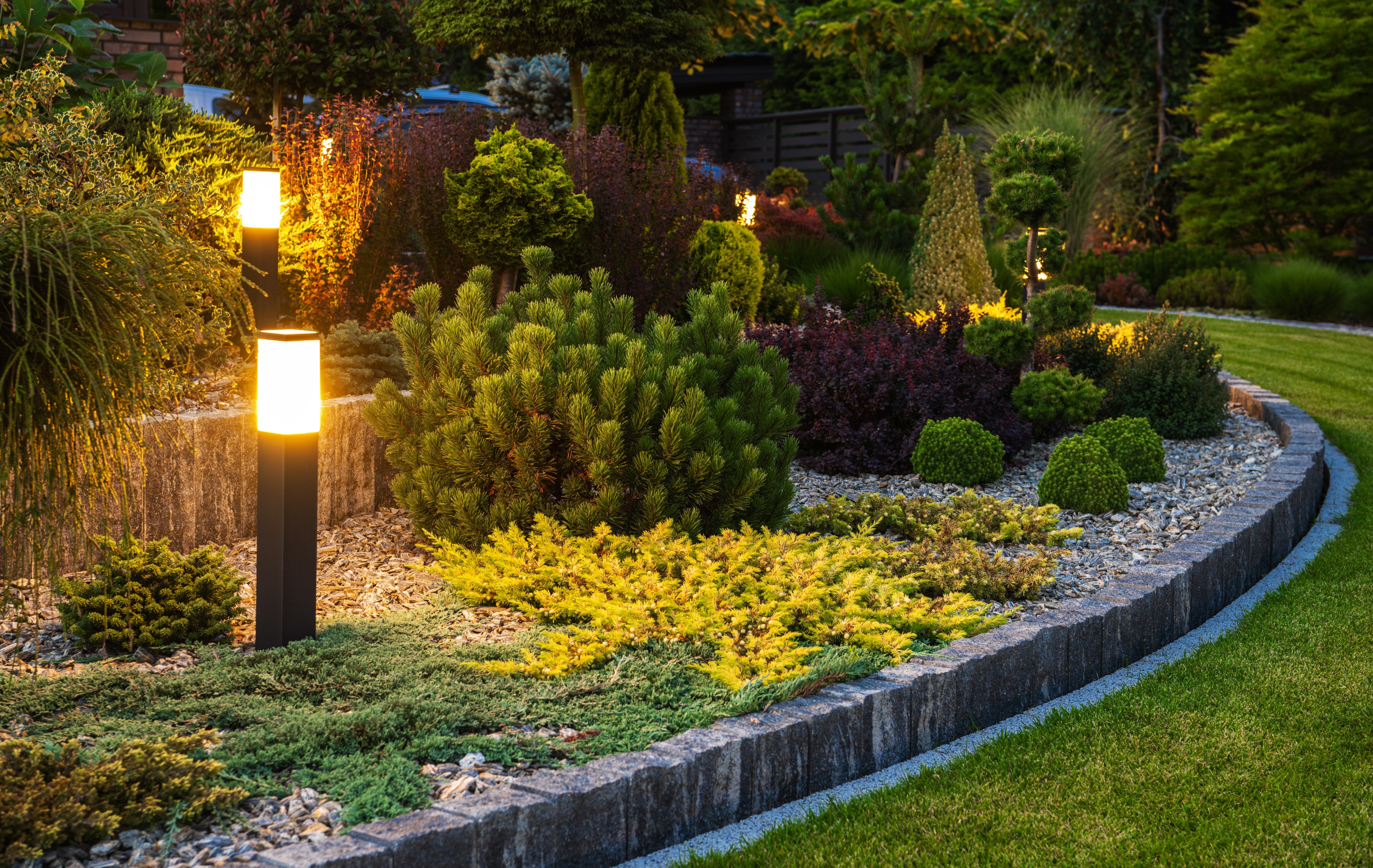 Luxury coastal home illuminated at evening twilight with warm landscape lighting against deep blue dusk sky
