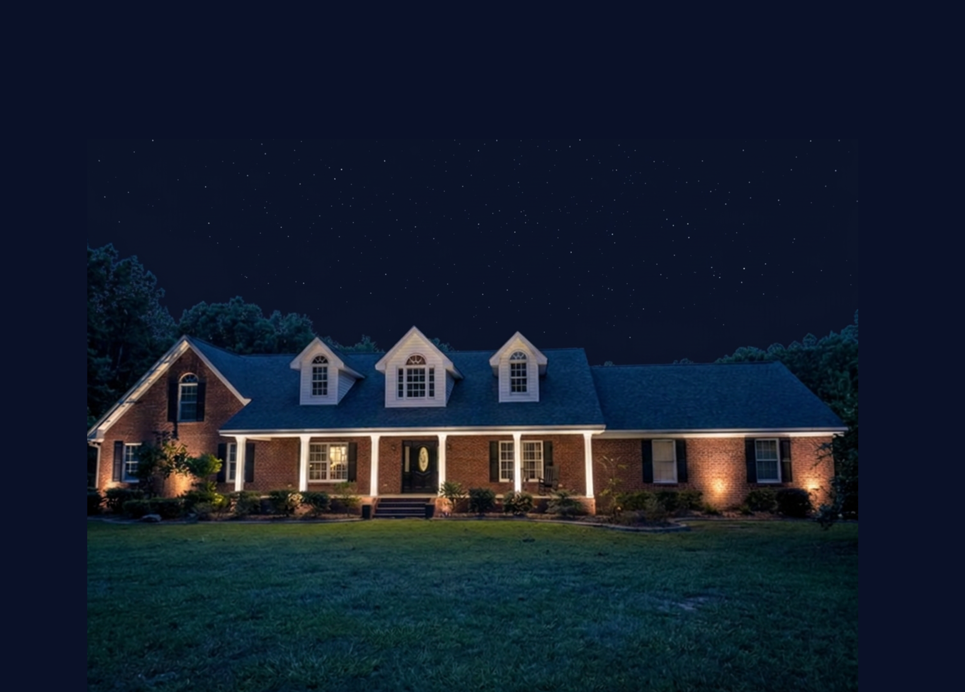 Coastal home driveway entrance with illuminated stone pillars and landscape lighting