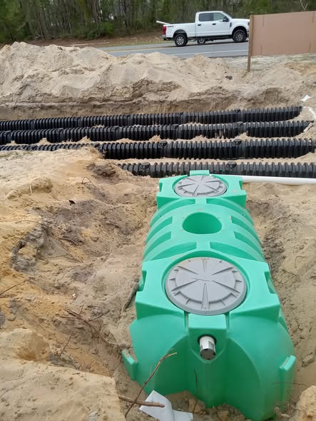 Professional Midstate Waterworks crew operating a yellow excavator installing an underground septic tank on a residential property with fresh dug trenches and irrigation piping