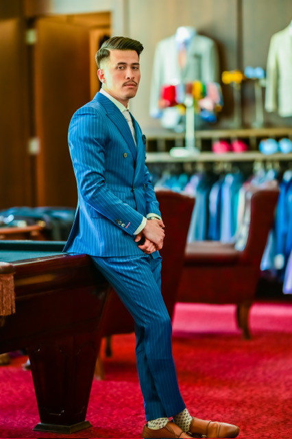 Master tailor conducting a bespoke fitting with premium luxury fabric swatches and finished custom suits for men and women in an elegant private atelier setting