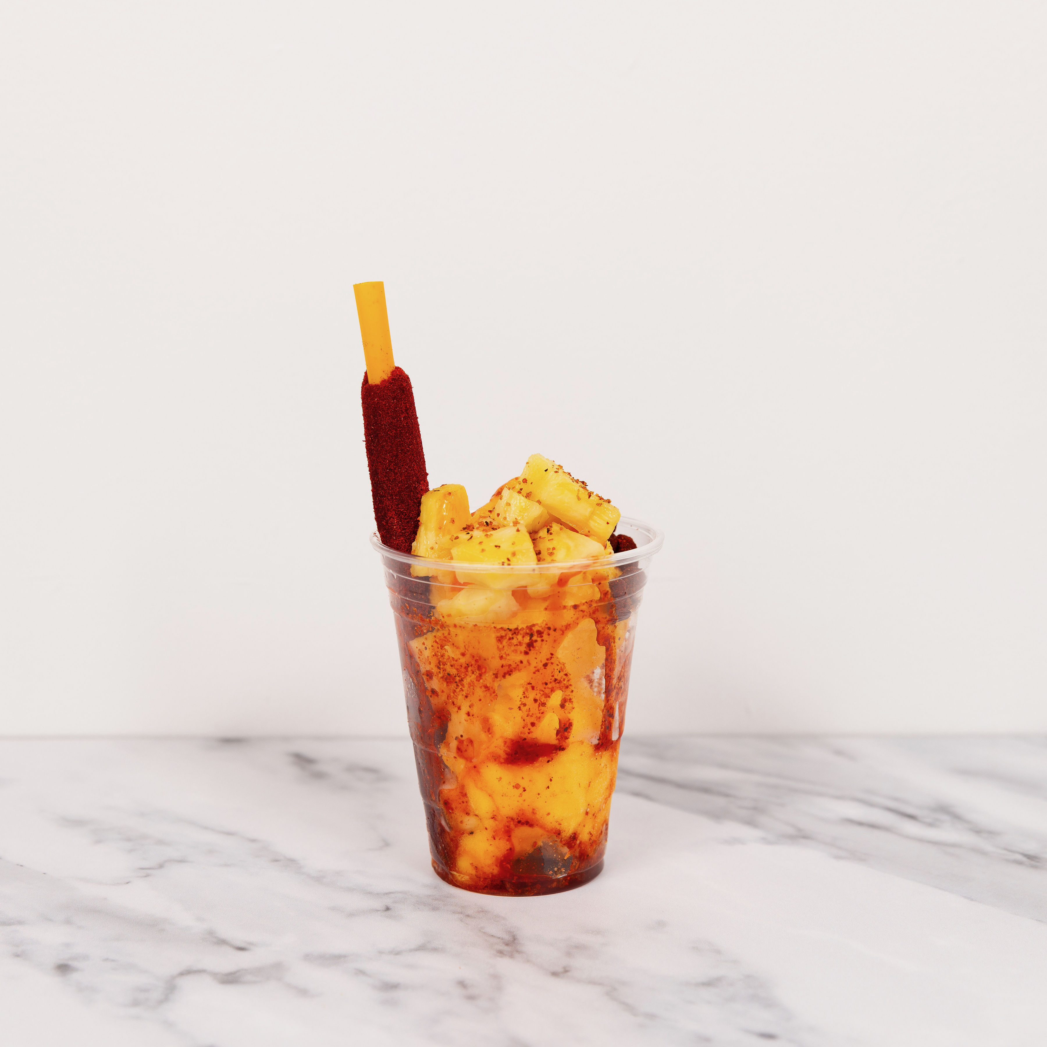 A close-up of a vibrant orange mangonada with a tamarind straw and chamoy drizzle