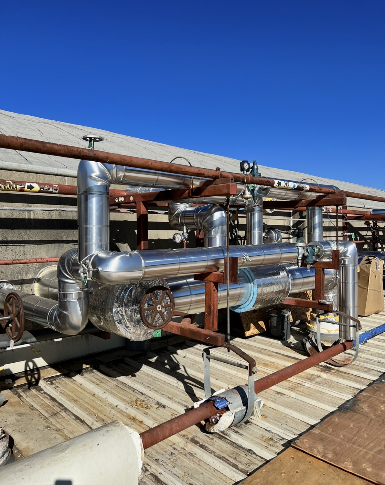 Insulated high-pressure steam lines running through an oil refinery with polished aluminum jacketing and elbow fittings.