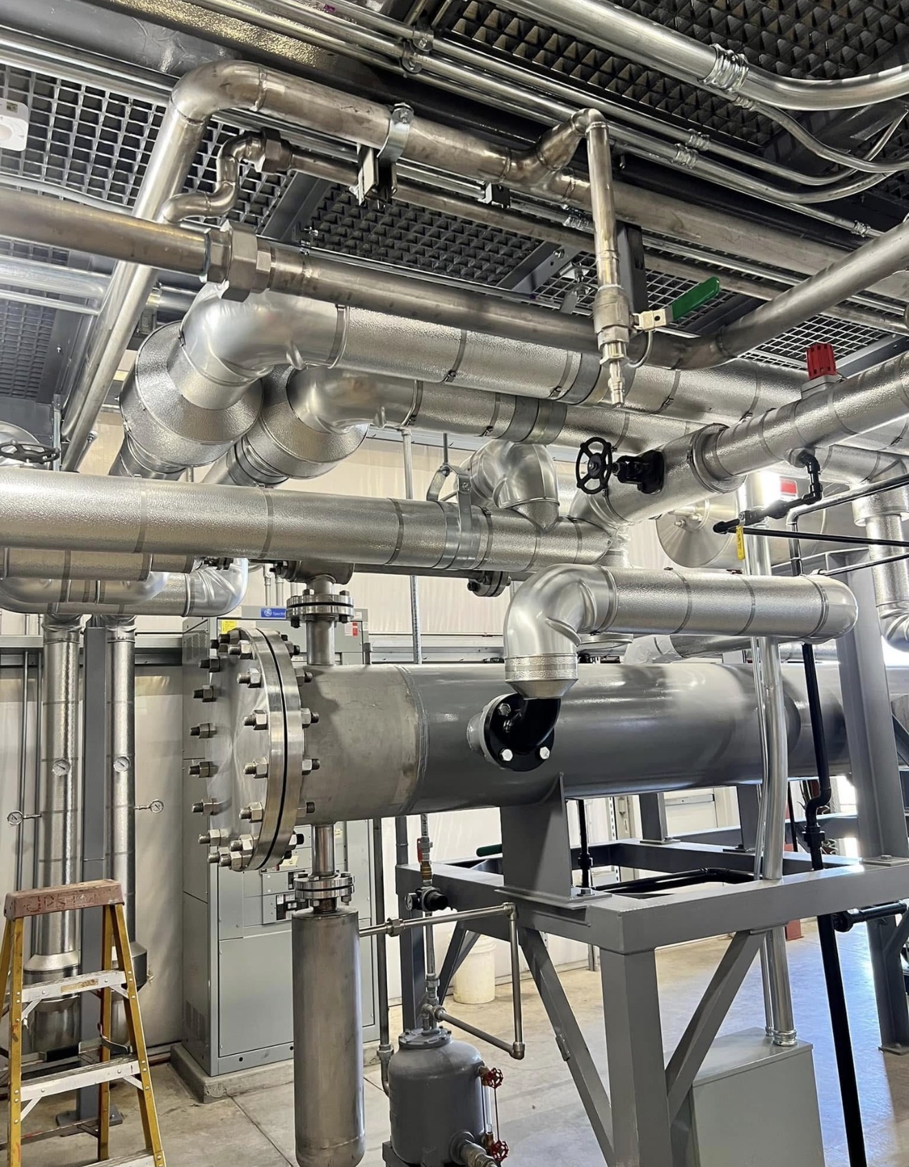 Cold storage warehouse ceiling pipes wrapped in thick closed-cell foam insulation with vapor barrier to prevent condensation.