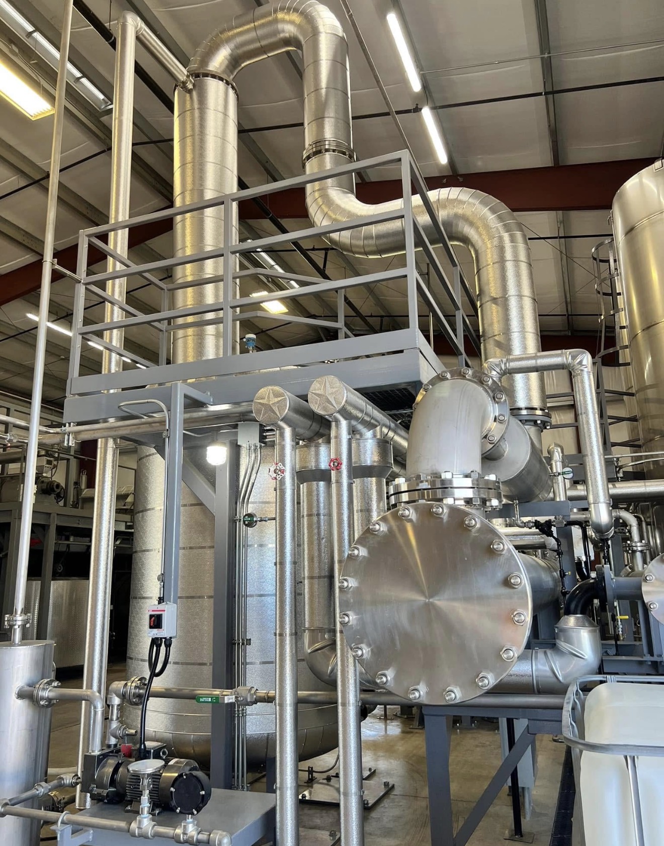 Certified insulation technician in safety gear installing thermal insulation on large diameter process pipes at an industrial facility.