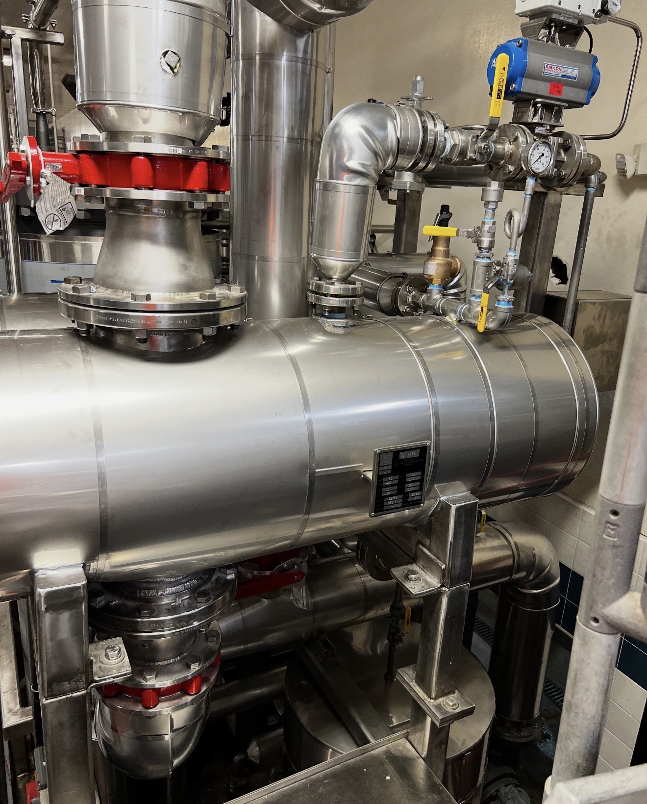 High-temperature hot oil process lines wrapped in calcium silicate insulation and finished with smooth polished aluminum cladding running along an industrial pipe rack.