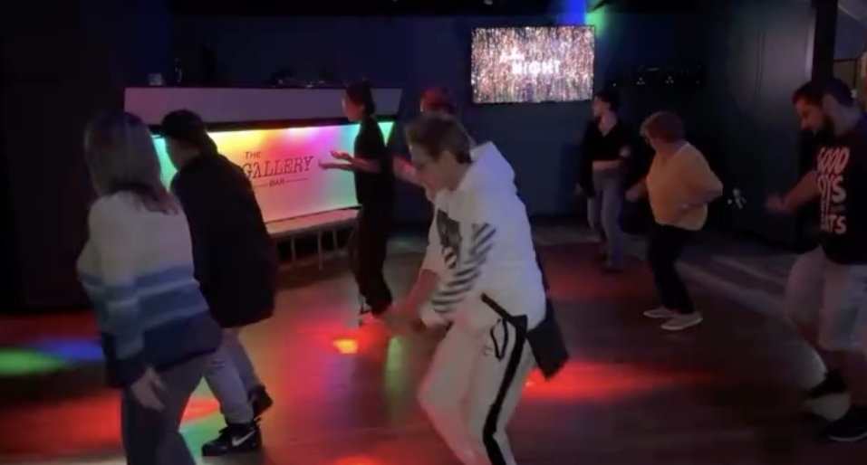 Crowd dancing and celebrating inclusivity under gold and pink lights at LGBTQ+ nightclub