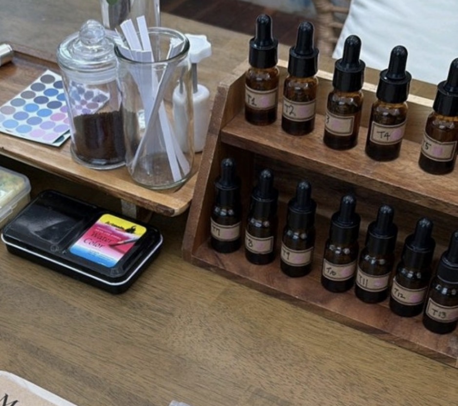 A beautifully arranged collection of small crystal perfume bottles surrounded by dried lavender, citrus peel, and local Jeju botanicals on a marble surface.