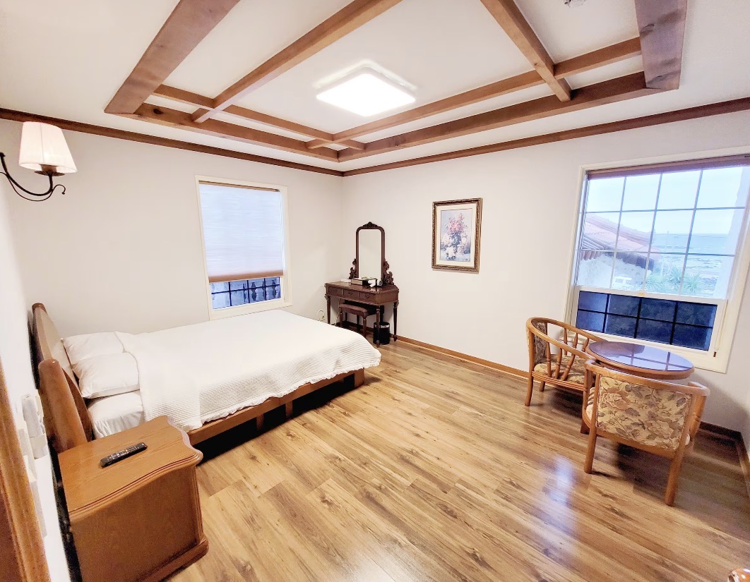 A spacious, light-filled private bedroom with a queen bed, soft linens, and serene minimalist decor in a Jeju ocean retreat.