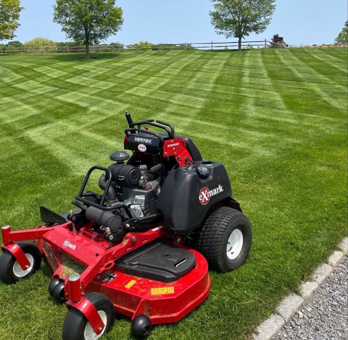 Freshly mowed vibrant green lawn with crisp edge trimming along concrete driveway and manicured shrub line in front of a two-story suburban home, completed by M&N Landscaping