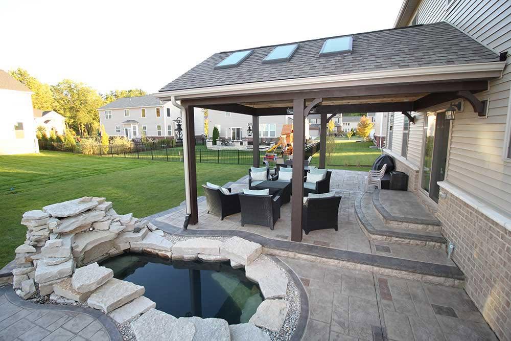 Covered patio with pergola, seating area, and stone-edged plunge pool in backyard
