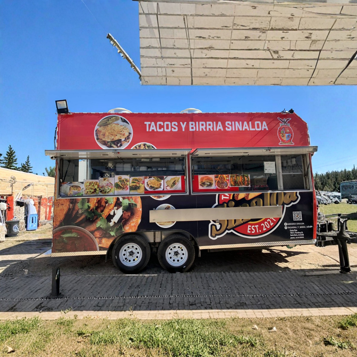 Front view of the original Tacos y Birria Sinaloa food truck with blue sky, entire truck and trailer fully visible