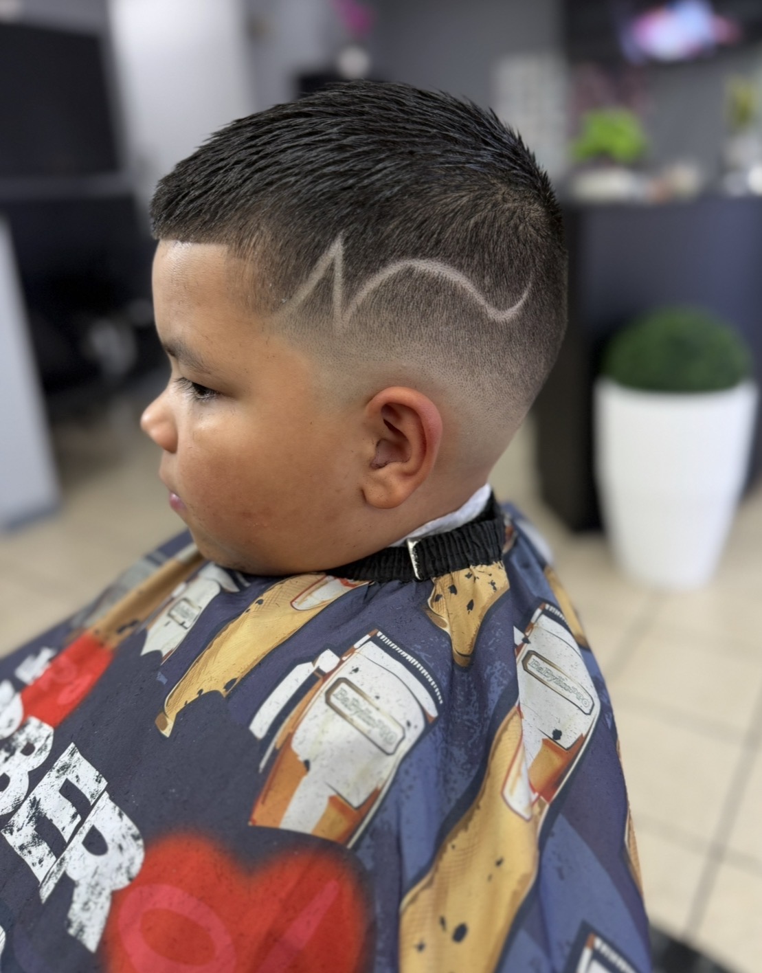 Authentic KARY HAIR SALON photo of young child getting a fresh haircut in the salon chair with cape on, bilingual stylist working carefully, warm salon lighting