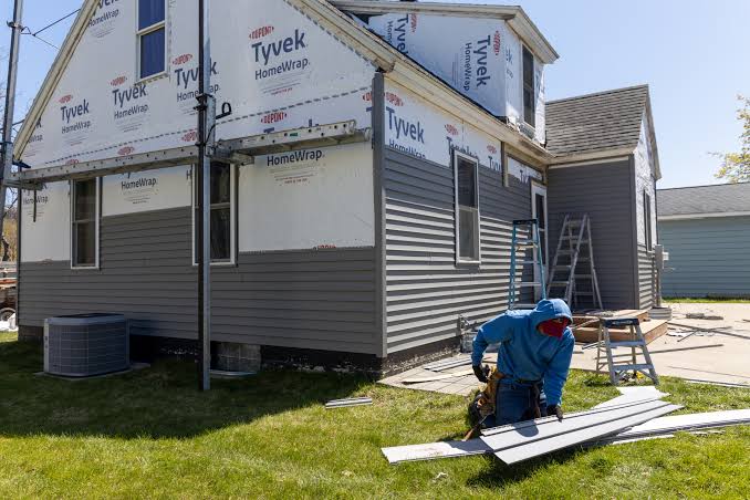 Professional installer applying new vinyl siding to the exterior of a suburban family home