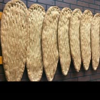 Fresh elongated Afghan naan bread being pulled from a hot traditional tandoor clay oven, golden brown crust with sesame seeds, steam rising