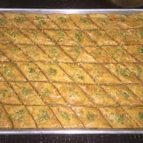 Colorful assortment of traditional Afghan sweet pastries including pistachio baklava, cardamom roat cookies, and rose-scented sweets arranged on golden trays