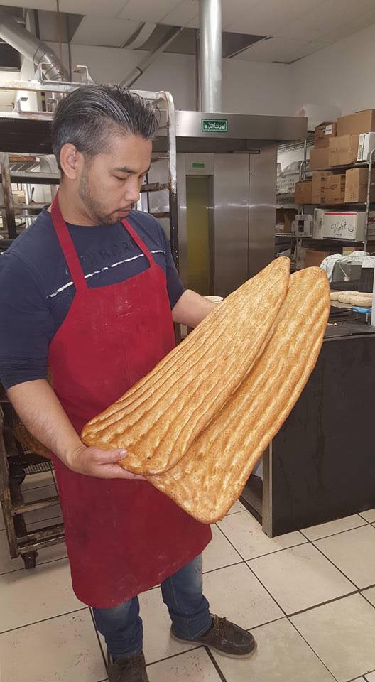 Afghan head baker and owner smiling in traditional bakery holding fresh naan bread