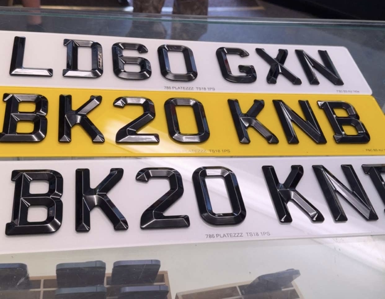 Classic retro black number plate with raised silver pressed metal characters mounted on a vintage restored car