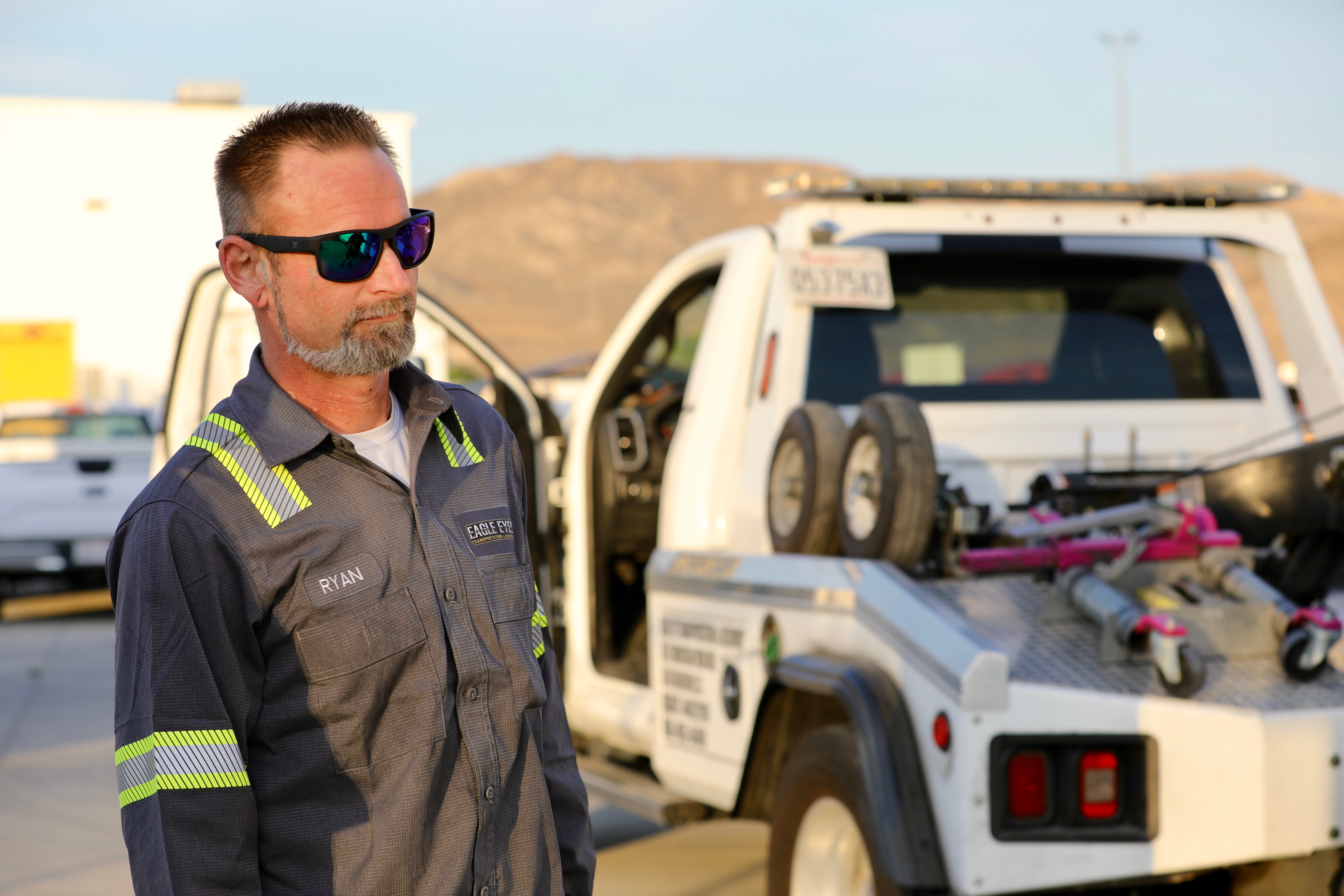 Friendly professional tow truck driver in uniform standing confidently next to a modern tow truck