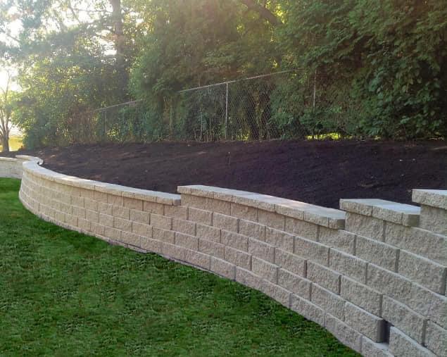 Beautifully constructed natural stone retaining wall with landscaped tiers and decorative rock features supporting a sloped garden with lush plantings
