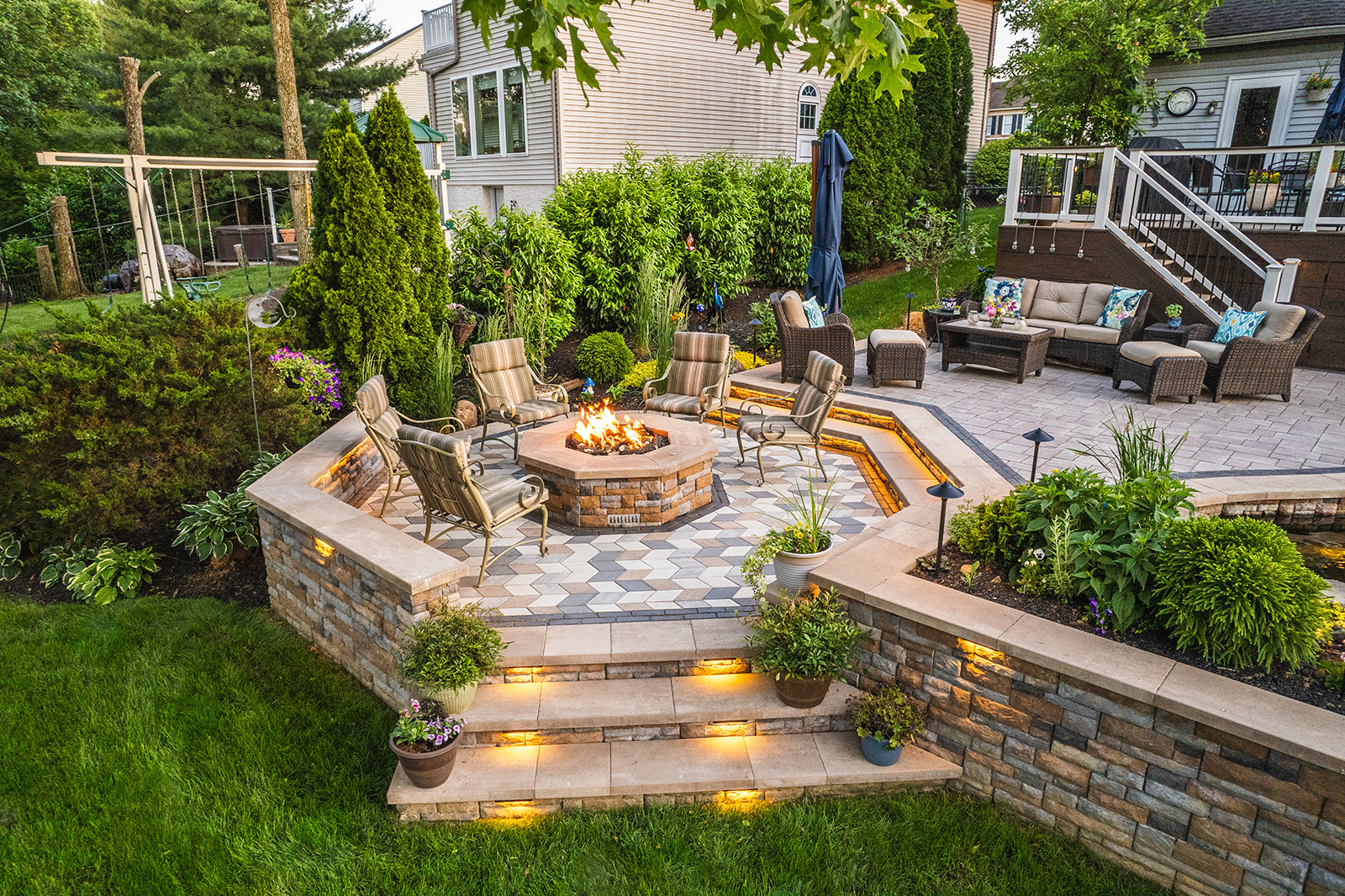 Modern backyard landscape by AGR featuring a custom stone patio, outdoor kitchen, and vibrant plantings