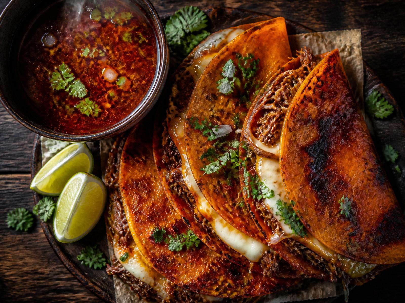 Colorful platter of authentic Mexican quesatacos with crispy tortillas, melted cheese, birria beef, fresh limes, radishes and salsa