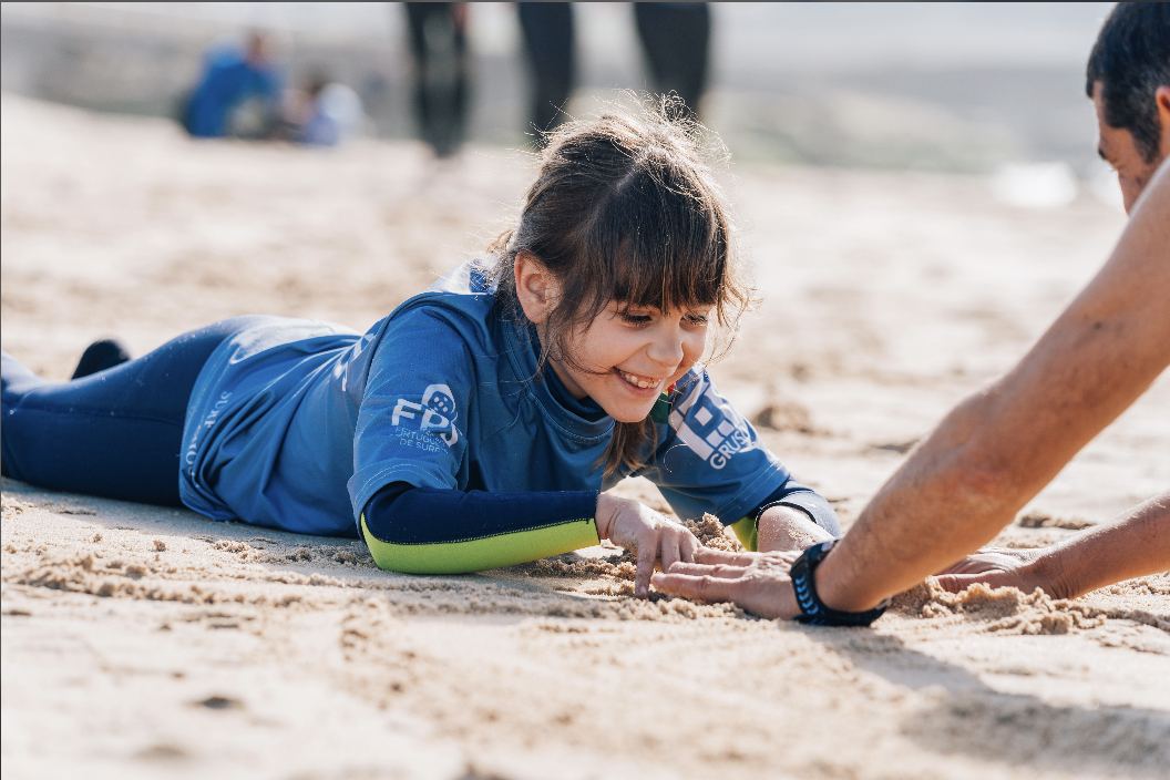 Surfista adaptado a deslizar numa onda em Carcavelos com o instrutor da Nossa Onda a apoiá-lo dentro de água